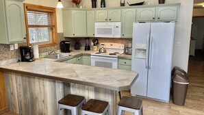 A kitchen with a central island, a refrigerator, and bar stools. - Four Seasons Vacation Home By Lake,  HOT TUB, WIFI,BEACH passes, Canoe, FIRE PIT (Lake Harmony)