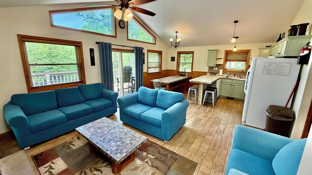 A spacious living area with a ceiling fan, two blue sofas, a patterned coffee table, and a kitchen area with a refrigerator and cabinets. - Four Seasons Vacation Home By Lake,  HOT TUB, WIFI,BEACH passes, Canoe, FIRE PIT (Lake Harmony)