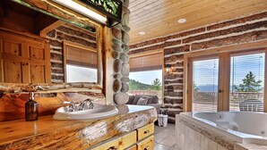 Une salle de bain rustique dans un chalet, avec un mur en pierre, des meubles en bois, un grand lavabo et une baignoire.