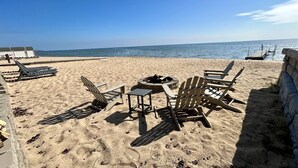 A beach with Adirondack chairs, a fire pit, and a view of the ocean.