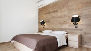 Un dormitorio moderno con cabecera de madera, cama con colcha marrón, dos mesitas de noche con lámparas negras y una pequeña cómoda.