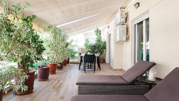 Un patio techado con sillones de mimbre, plantas en macetas y una mesa de comedor.