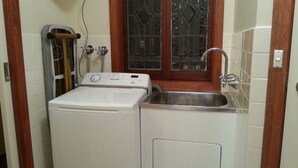 Un espace buanderie compact comprenant un lave-linge, un évier et une fenêtre ornée de vitraux.