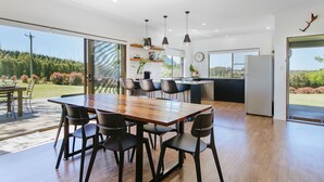 Une cuisine moderne avec une grande table à manger, des chaises noires, des luminaires suspendus et une vue sur l’extérieur.
