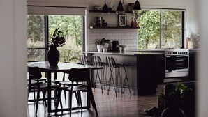 Une cuisine moderne dotée d’une grande fenêtre, d’une table à manger en bois et de tabourets de bar.