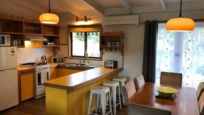 A compact kitchen with a central island, bar stools, a dining table, and a view of the outdoors. - CHA CHA - Pet Friendly-Netflix WiFi  (Inverloch)