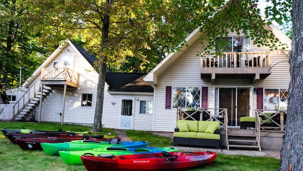 Una casa con un portico coperto e una scala che conduce a un patio. Diverse canoe sono allineate davanti alla casa.
