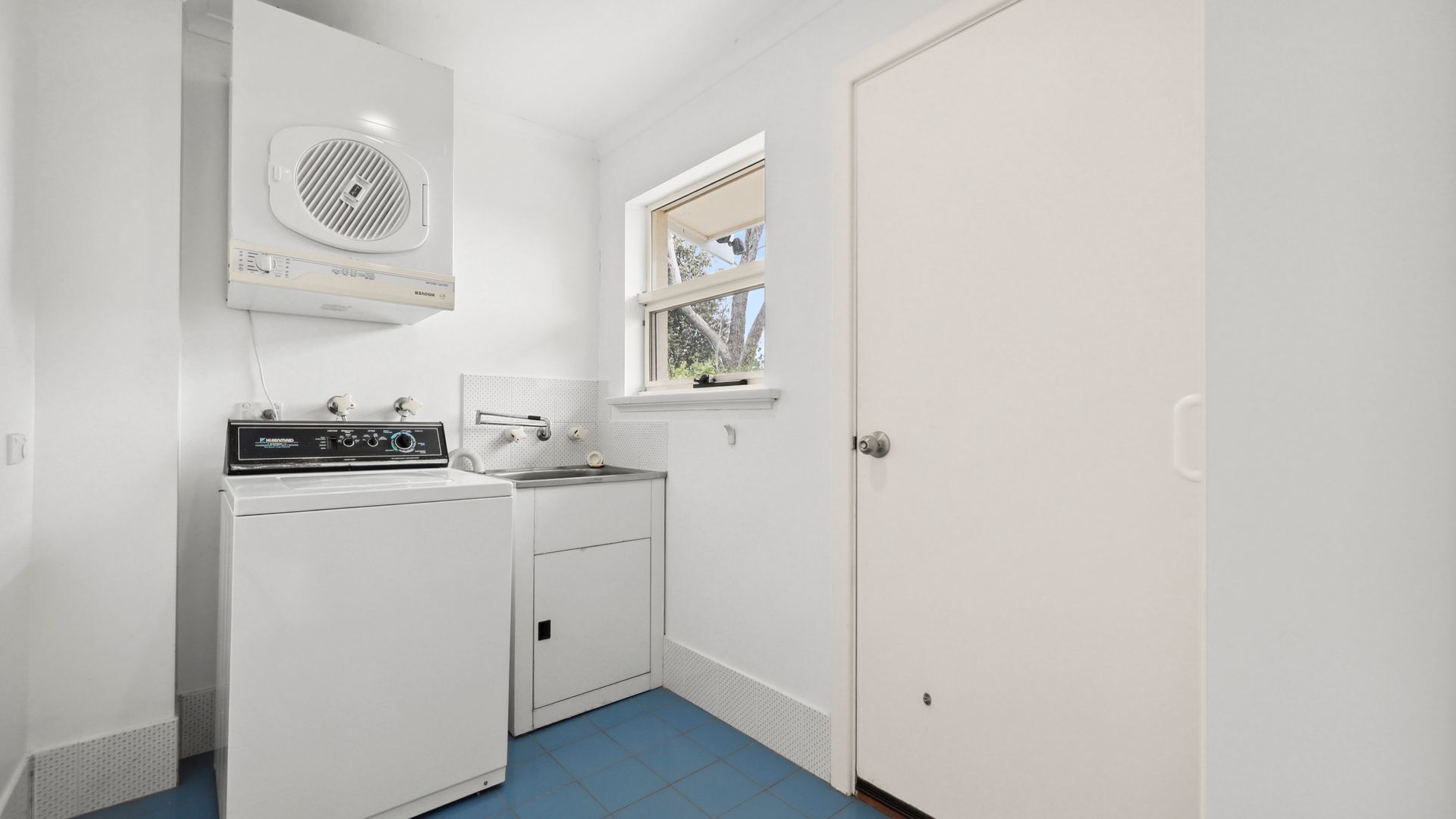 Een wasserette met een wasmachine, droger en ventilatiesysteem.