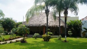 Un bâtiment à toit de chaume, entouré d’une pelouse bien entretenue et de palmiers.