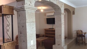 Un salon avec une colonne en pierre, un téléviseur fixé au mur et une table en bois.