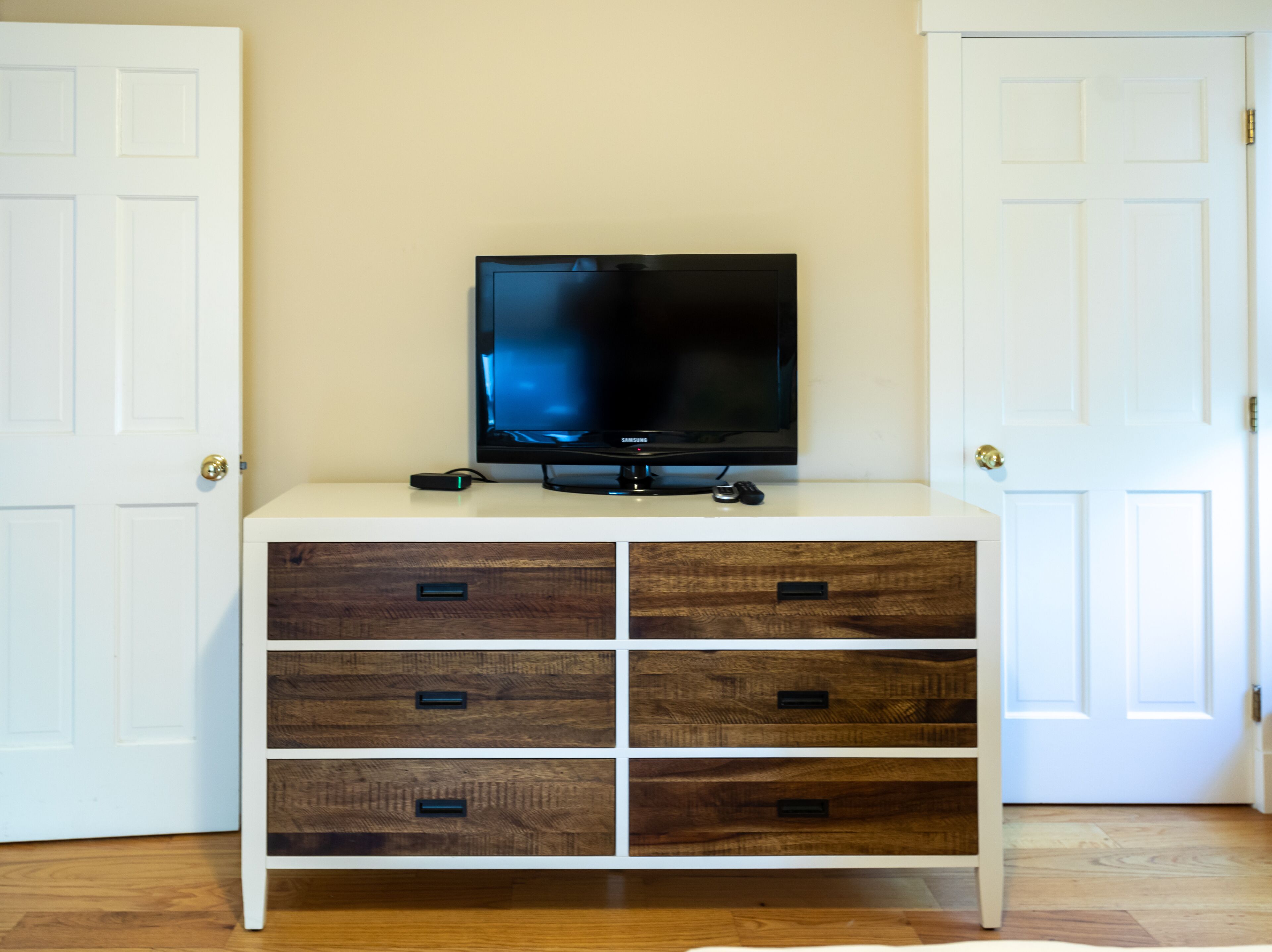 A television on a white cabinet with six drawers, located between two white doors.