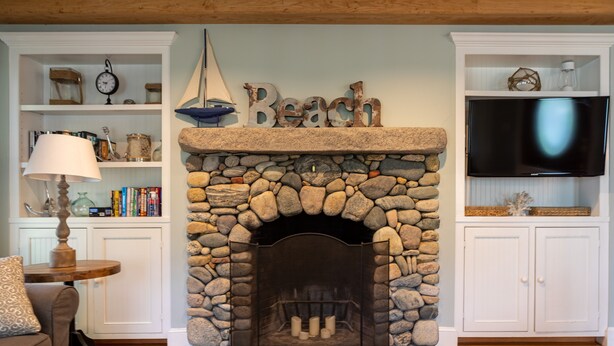 A living room with a stone fireplace, a bookshelf, a television, and a cozy seating area. - Quintessential MV home near Oak Bluffs, beach & harbor (Oak Bluffs)