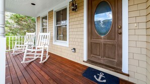 A porch with rocking chairs, a wooden door with a glass panel, and a view of trees and sky. - Quintessential MV home near Oak Bluffs, beach & harbor (Oak Bluffs)