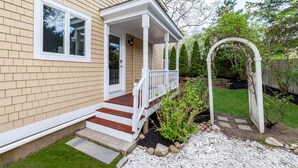 A house with a covered porch, a front door, and a small garden area with a wooden arbor. - Quintessential MV home near Oak Bluffs, beach & harbor (Oak Bluffs)