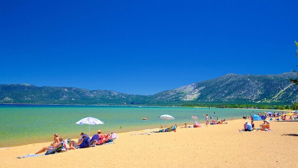 Una playa con gente relajándose, agua cristalina y montañas al fondo.