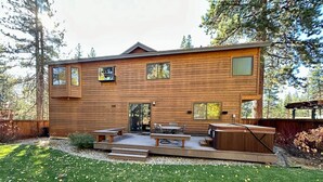 Una cabaña moderna de madera con terraza, asientos al aire libre y un ventanal grande.