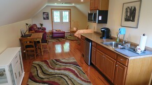A kitchen with wooden cabinets, a stainless steel refrigerator, and a microwave. There is a dining area with a table and chairs, and a living room with a couch and a chair. - Private Beach And  Mountain Lake Home (Washington)