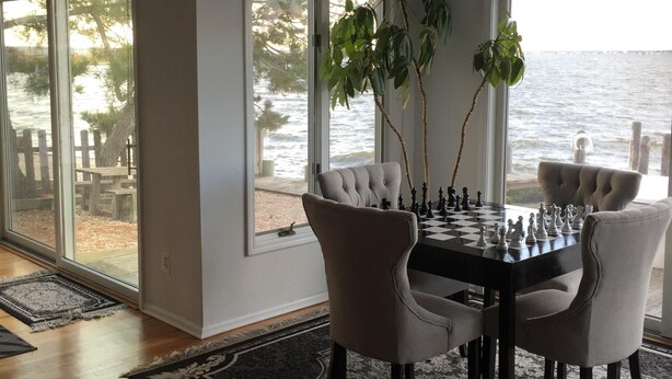A dining area with a chessboard, large windows, and a view of the water. - Gorgeous Waterfront Home with Spectacular Views! Book Your Getaway Now!  (Lavallette)