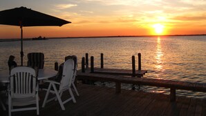 A wooden deck with white chairs and an umbrella, overlooking a sunset over water. - Gorgeous Waterfront Home with Spectacular Views! Book Your Getaway Now!  (Lavallette)