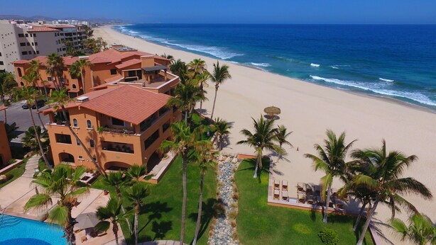 Ein Strandhotel mit mehreren Gebäuden, einem Schwimmbad und Palmen.