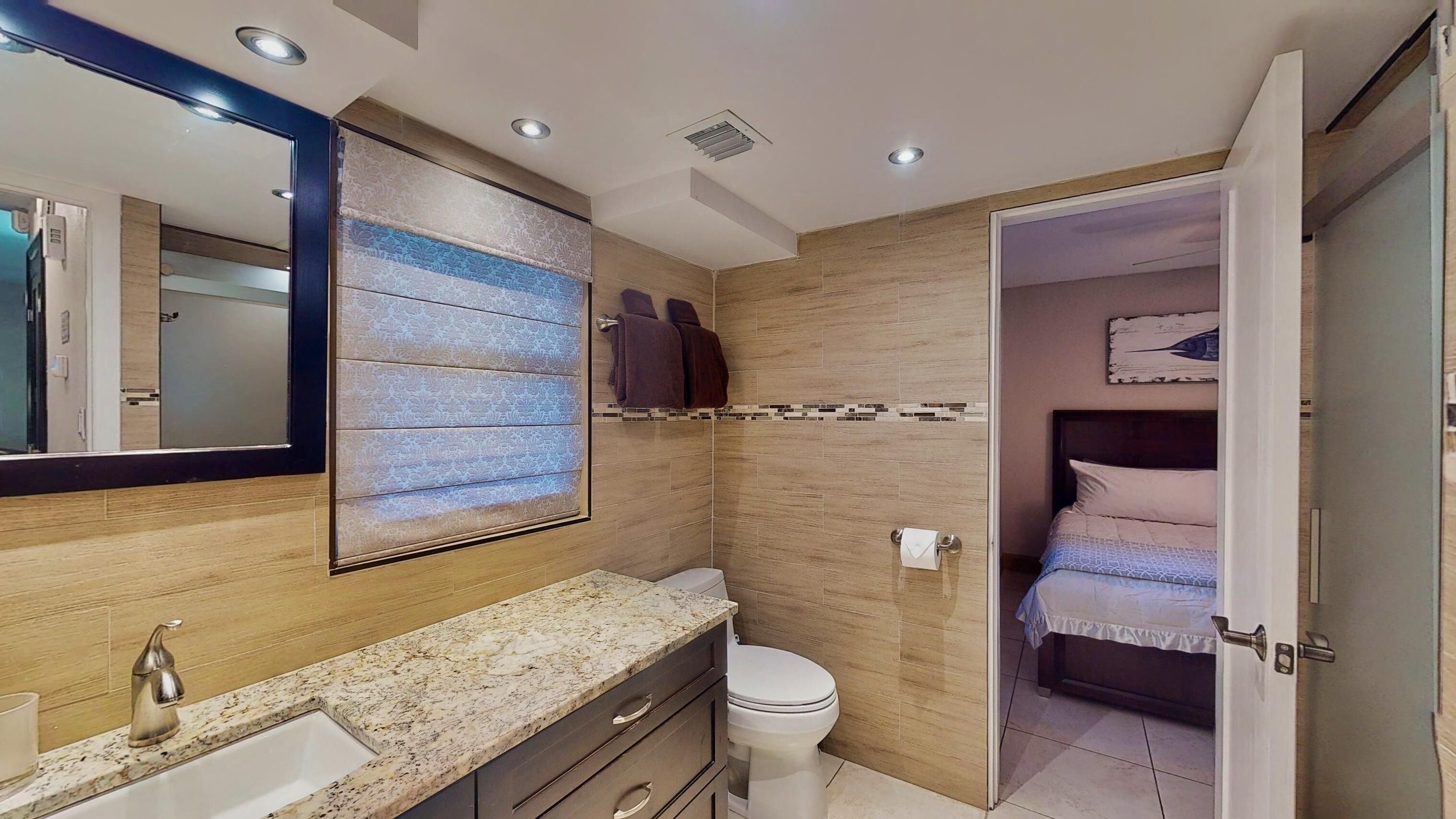 A modern bathroom with a granite countertop, a large mirror, and a wooden vanity.