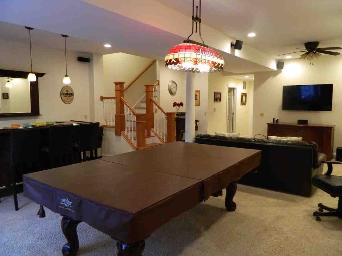 A billiards table in a room with a staircase, a television, and a ceiling fan.