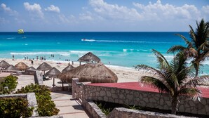 A beach resort with thatched-roof structures, a palm tree, and a clear view of the ocean. - A WINDOW TO PARADISE (Cancún)