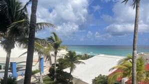 A beach view with palm trees, a clear sky, and a calm sea. - A WINDOW TO PARADISE (Cancún)