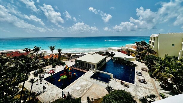 A resort with a pool area, palm trees, and a view of the ocean. - A WINDOW TO PARADISE (Cancún)