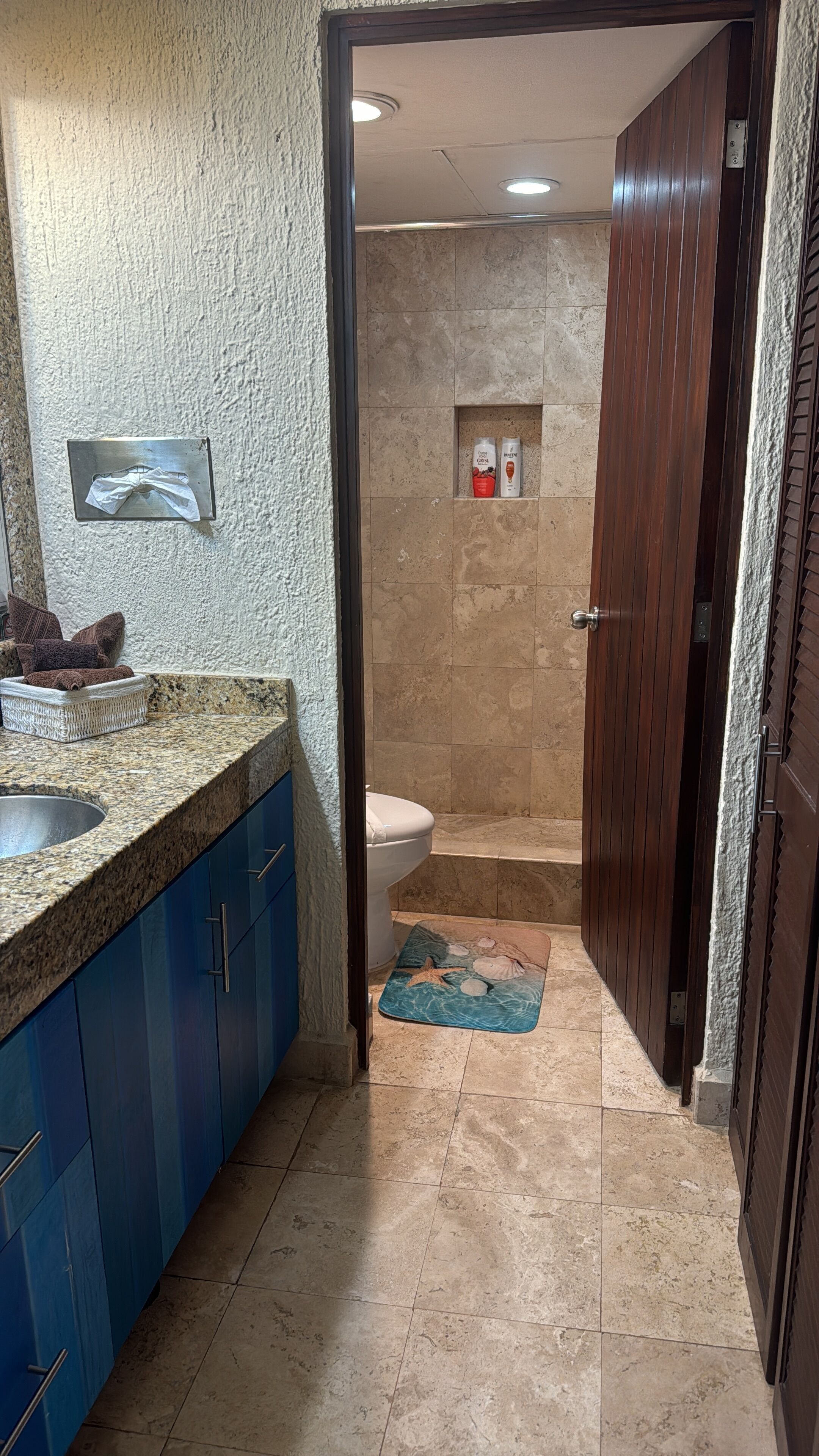 A bathroom with a marble sink, blue cabinets, a shower area, and a towel rack.