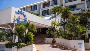 A hotel entrance with a modern design, including a distinctive blue and yellow logo, a covered walkway, and a landscaped area with palm trees. - A WINDOW TO PARADISE (Cancún)