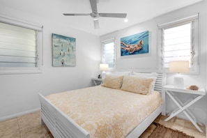 A bedroom with a bed, two nightstands, a ceiling fan, and artwork on the walls.