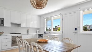 Une cuisine moderne avec des meubles blancs, une table à manger en bois et une vue sur le quartier.