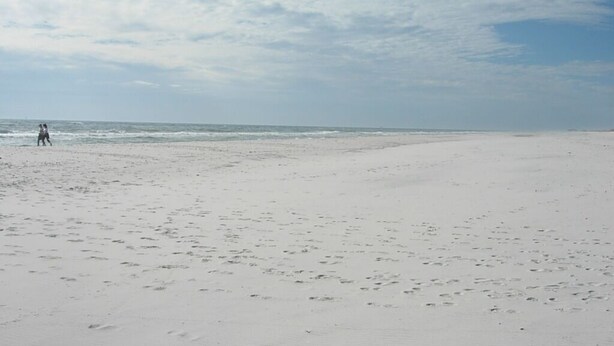 Ein weiter Sandstrand mit Fußabdrücken und blauem Himmel.