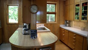 Una cocina con armarios de madera, un lavabo, un reloj y una cafetera.
