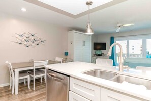Eine moderne Küche mit Geschirrspüler, ein Essbereich mit Stühlen, einem Deckenventilator und Blick auf einen Balkon.