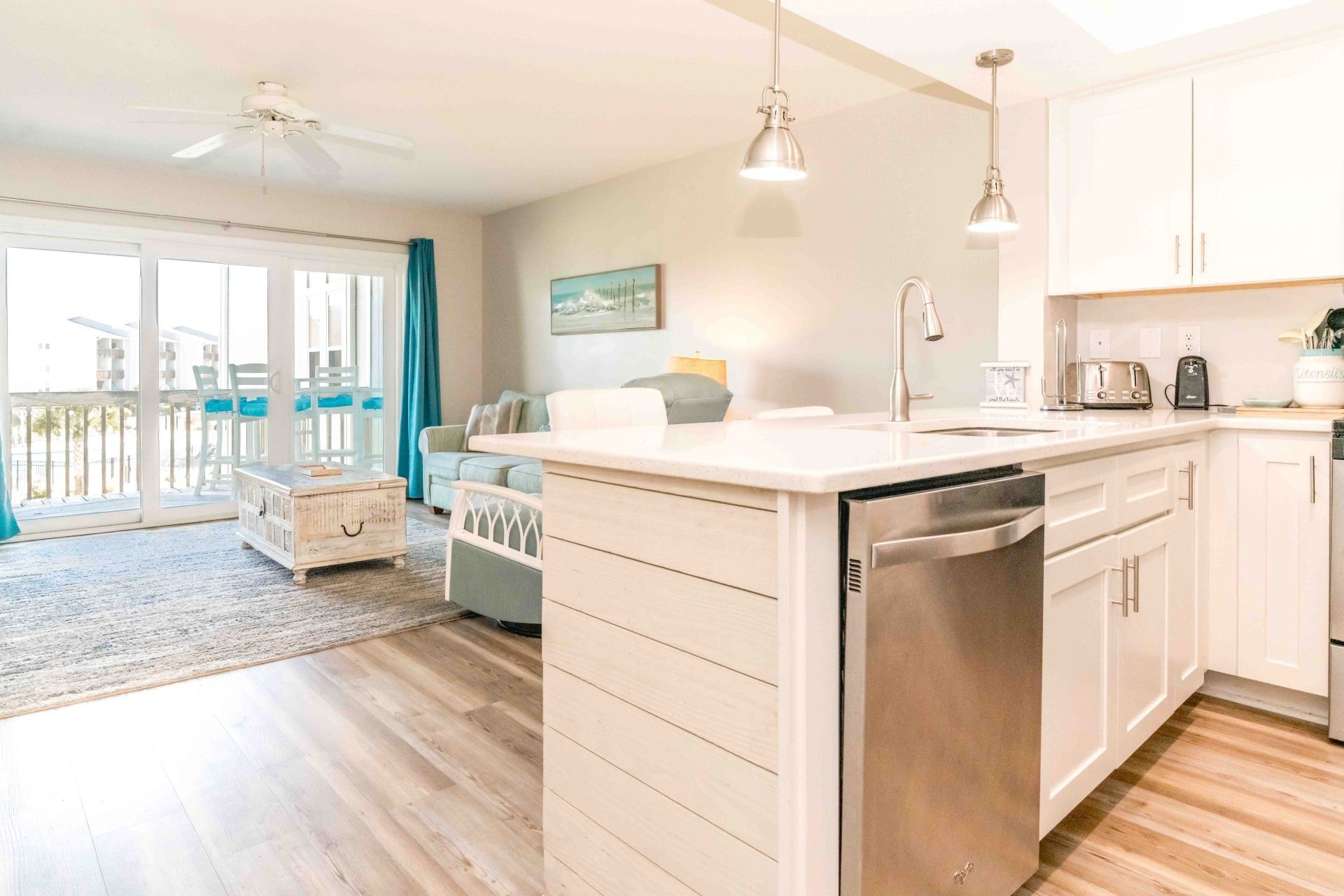 A modern kitchen with a dishwasher, a sink, and a countertop. There is a dining area with a sofa and a table.