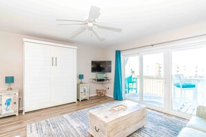 A spacious room with a ceiling fan, a sliding glass door leading to an outdoor area, a television mounted on the wall, and a wooden chest of drawers.