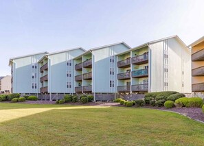 Ein mehrgeschossiges Wohngebäude mit Balkonen, einer flachen Dachterrasse und einem gepflegten Rasen.