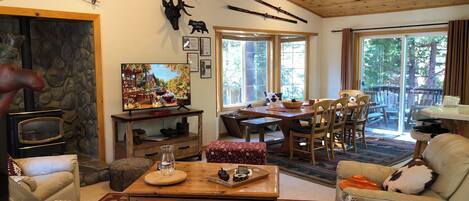 A cozy living room with a stone fireplace, wooden ceiling, and a deer head mounted on the wall.