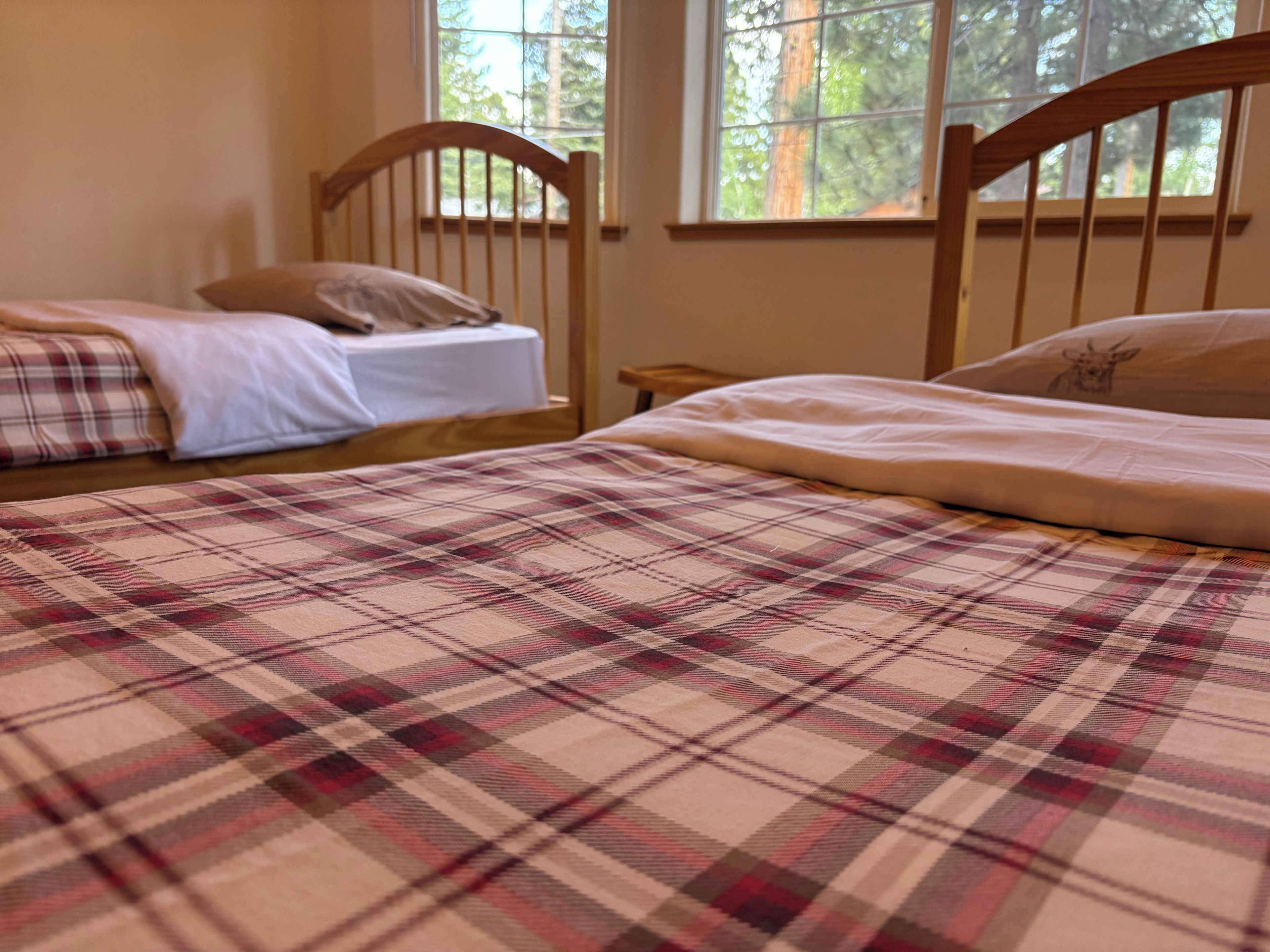 A bedroom with two beds, one with a plaid bedspread and the other with plain bedding.