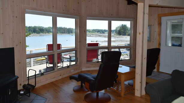 A room with large windows overlooking a lake, a wooden floor, a black chair, and a television.
