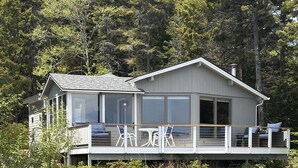 A two-story house with a deck overlooking a body of water, surrounded by trees.