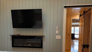 A bedroom with a bed, a TV mounted on the wall, and a sliding door leading to another room.