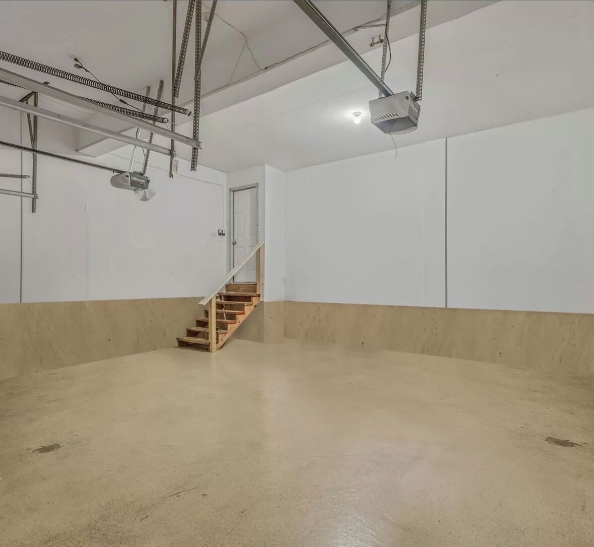 Ein geräumiger, leerer Raum mit Betonboden, einer Holztreppe und weißen Wänden.