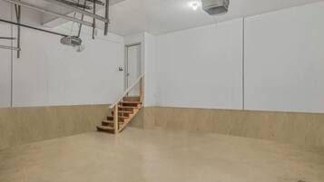 Ein geräumiger, leerer Raum mit Betonboden, einer Holztreppe und weißen Wänden.