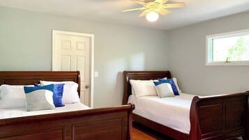 A bedroom with two wooden beds, a ceiling fan, a window with a view, and a door.