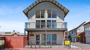 Un immeuble de deux étages doté d’un balcon à l’étage supérieur, d’une porte de garage et d’une enseigne indiquant qu’il propose des locations de vacances.