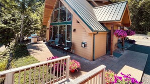 A modern cabin with a sloped roof, large windows, and a deck area with outdoor seating.