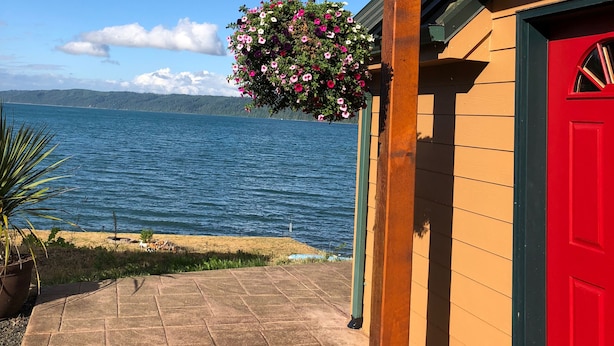 A wooden building with a red door, a hanging flower basket, and a view of a lake.